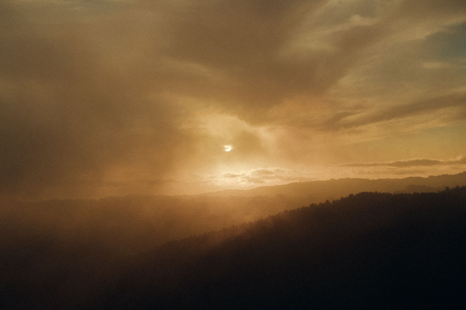 Dramatic golden sunset over mountain silhouettes with misty atmosphere.