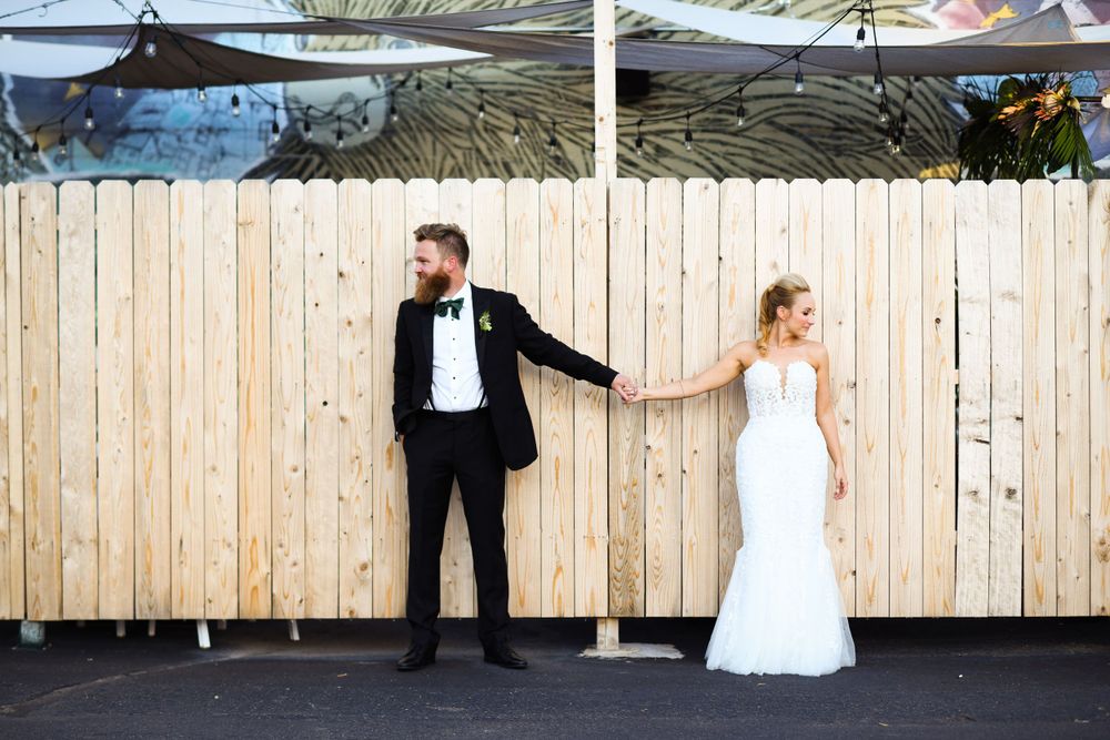 Creative wedding photo of couple on opposite sides of wooden fence in formal attire.