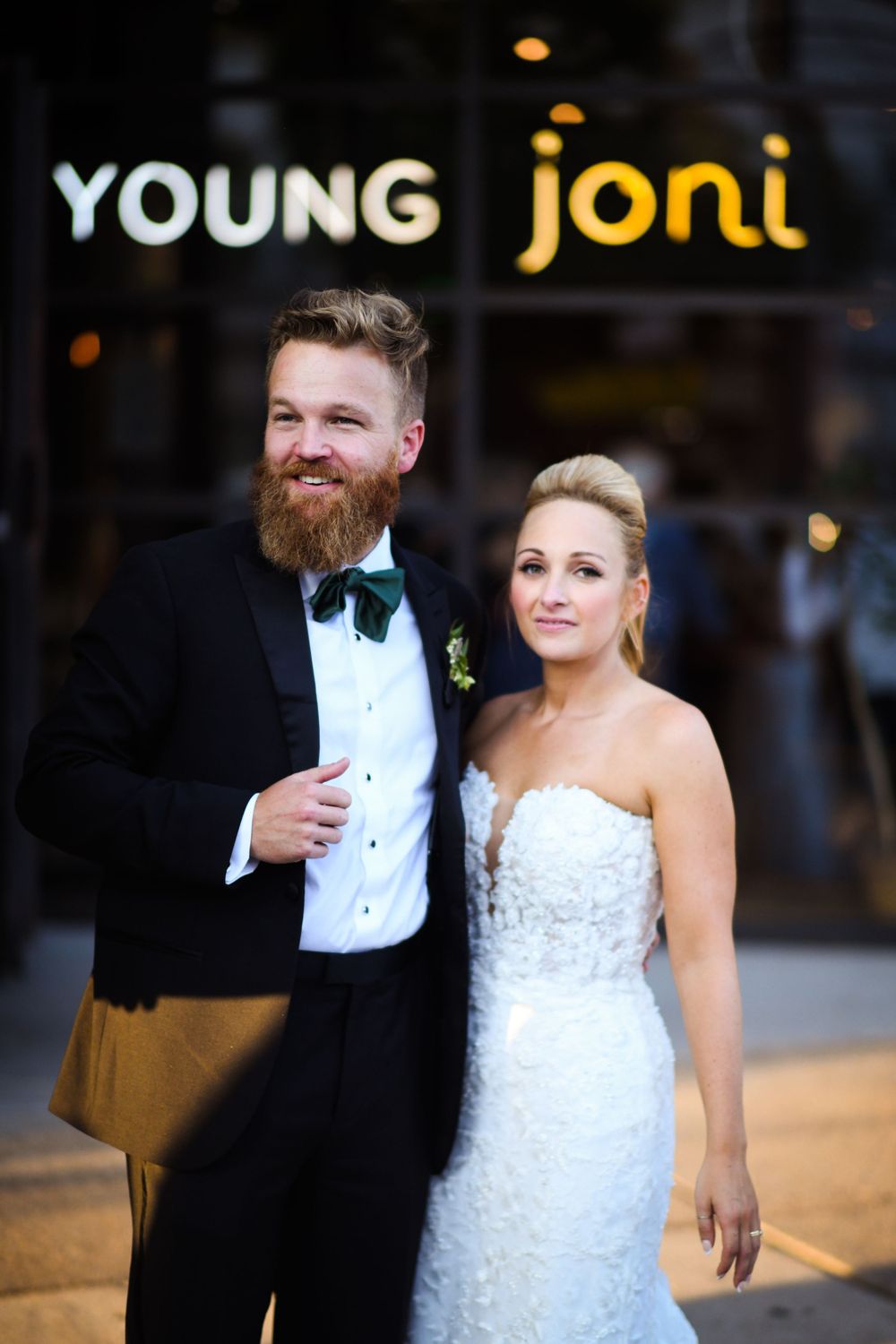 Wedding couple poses in formal attire outside Young Joni restaurant at night.