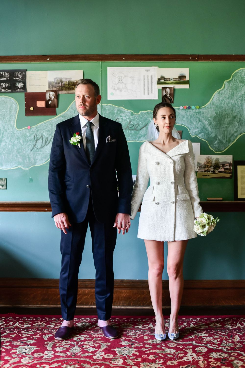 Couple in formal attire posing against green wall with vintage maps and decor.