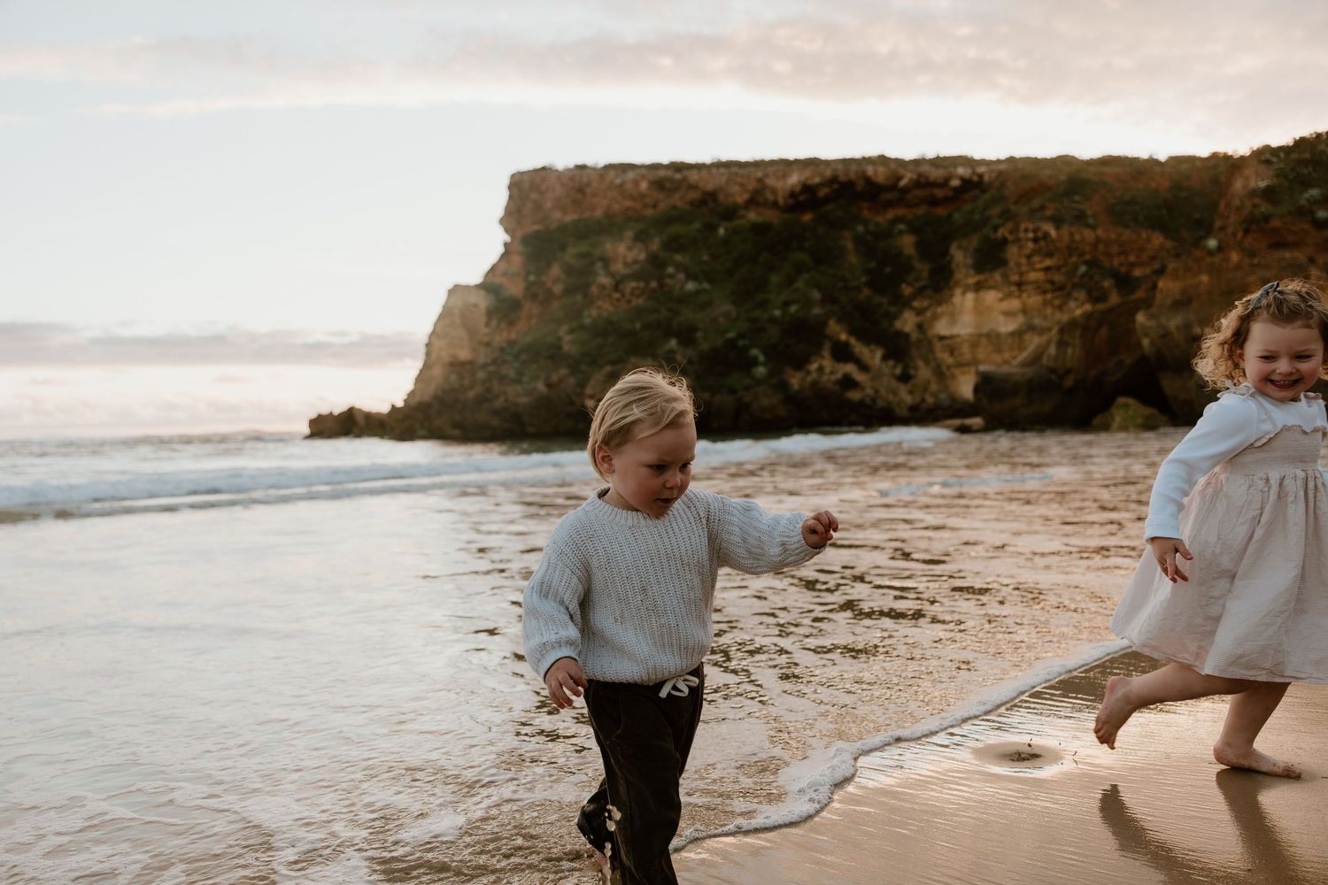 Young child running through tall grass field wearing white sweater.