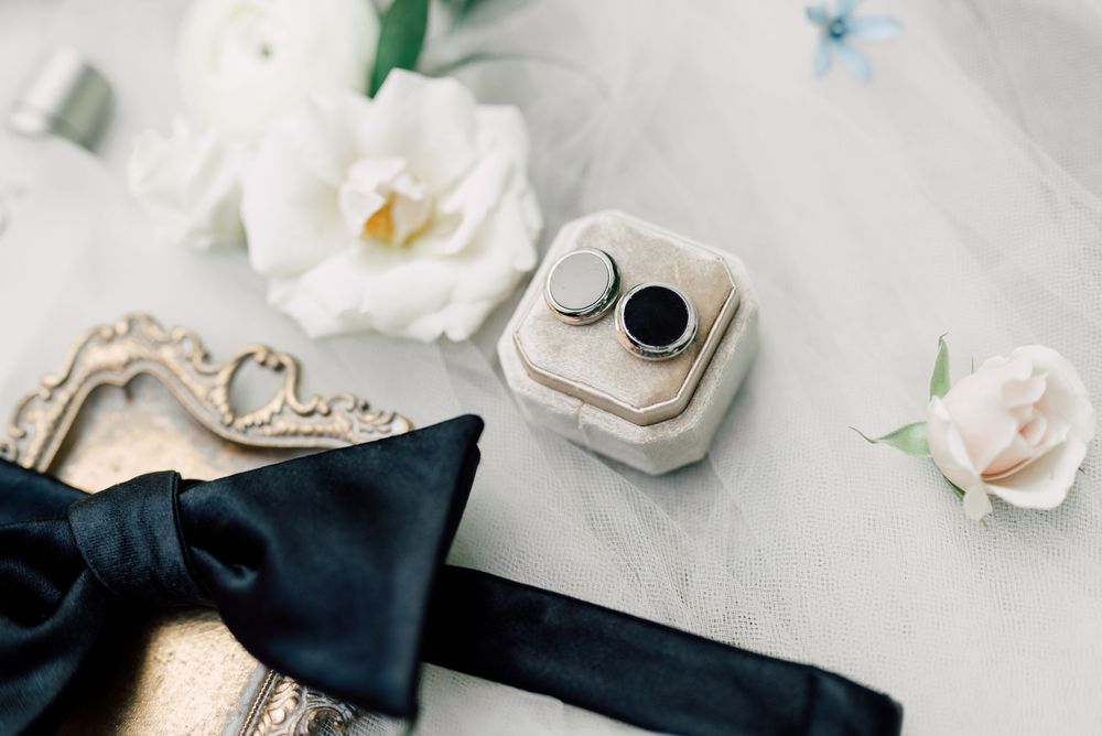 Wedding detail flatlay with white flowers, black ribbon, and delicate accessories on light background