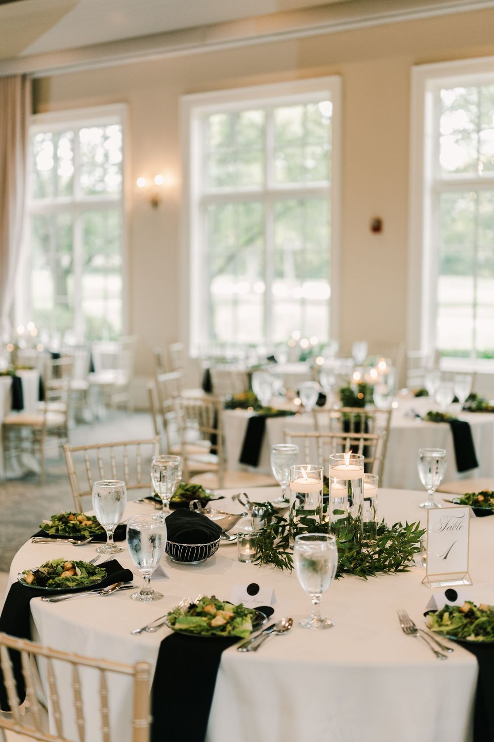 Elegant wedding reception setup with white tablecloths, greenery centerpieces and chiavari chairs at the pinnacle golf club