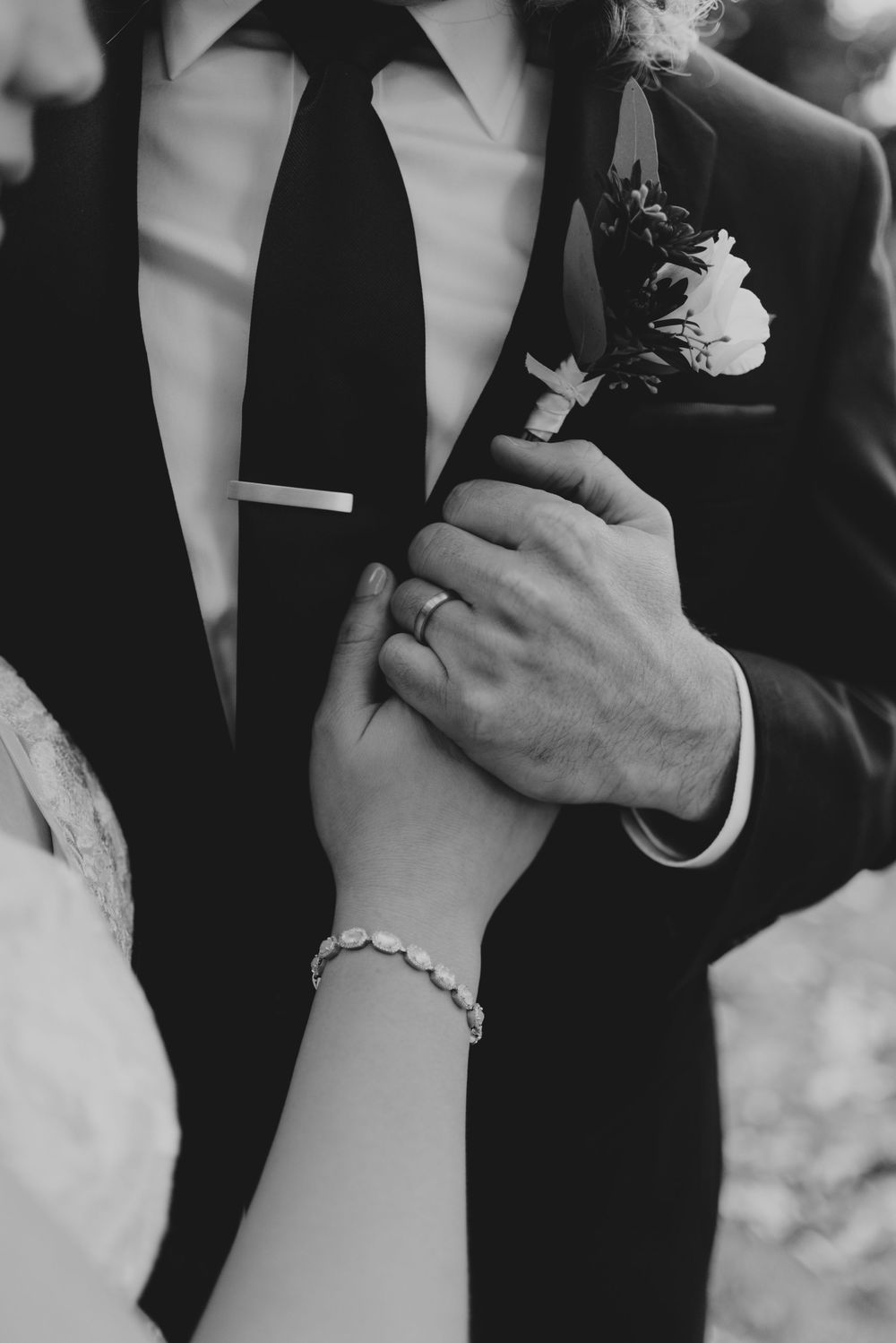 Black and white close-up photo showing hands clasped together during a romantic wedding moment
