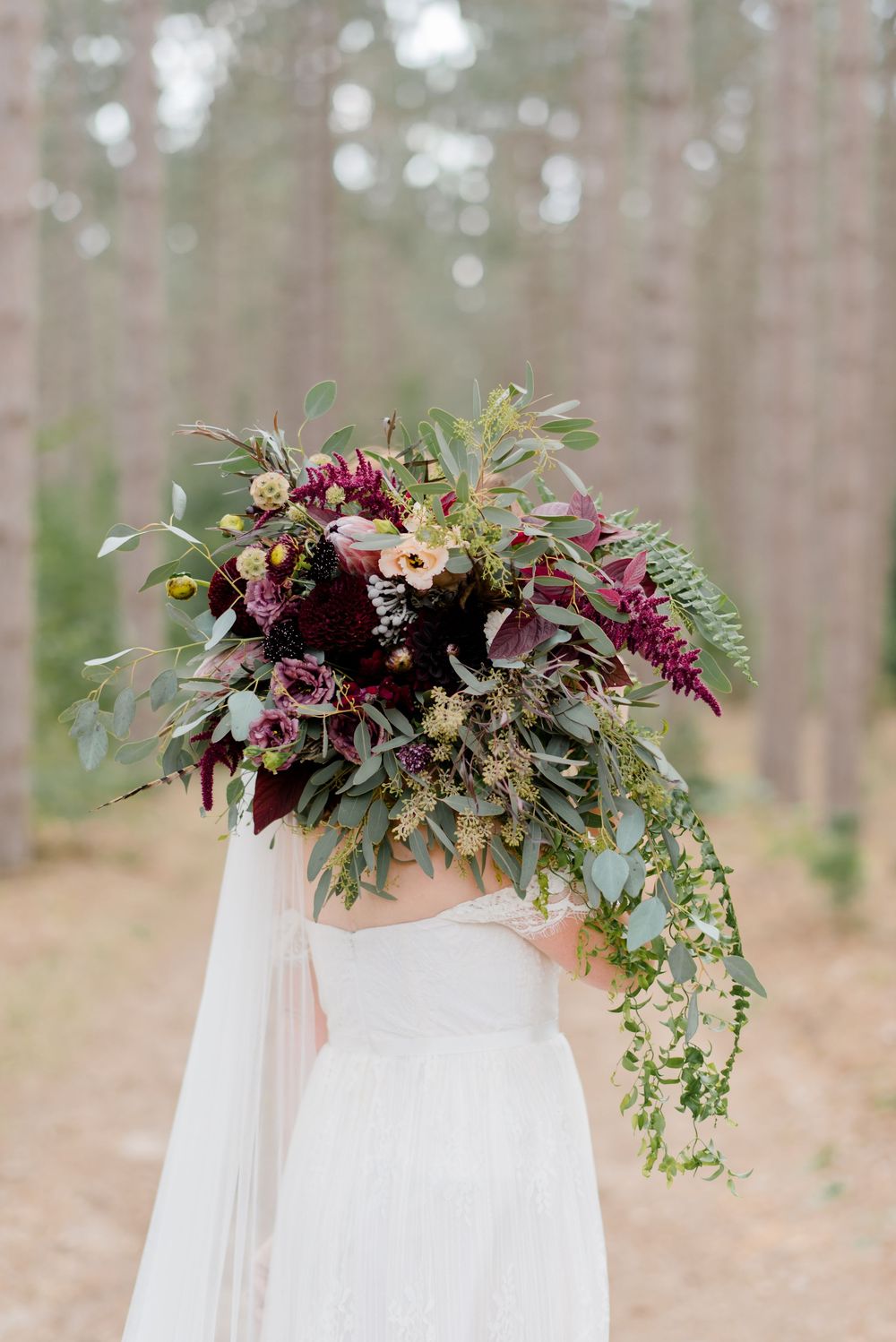 Cascading bridal veil decorated with burgundy and green floral arrangement in forest setting outdoor wedding in michigan