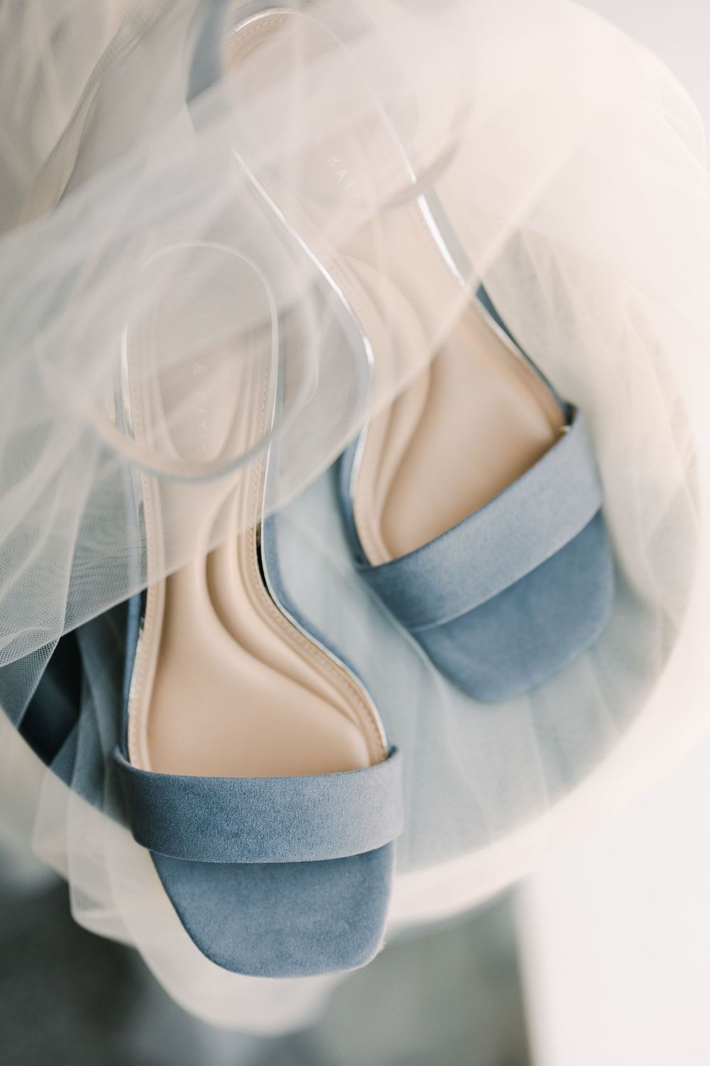 Blue suede block heel wedding shoes draped with a sheer bridal veil on a light background.