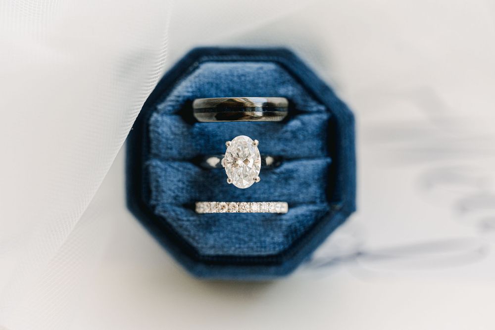 Oval diamond engagement ring with wedding band and eternity ring displayed in a blue velvet octagonal ring box.