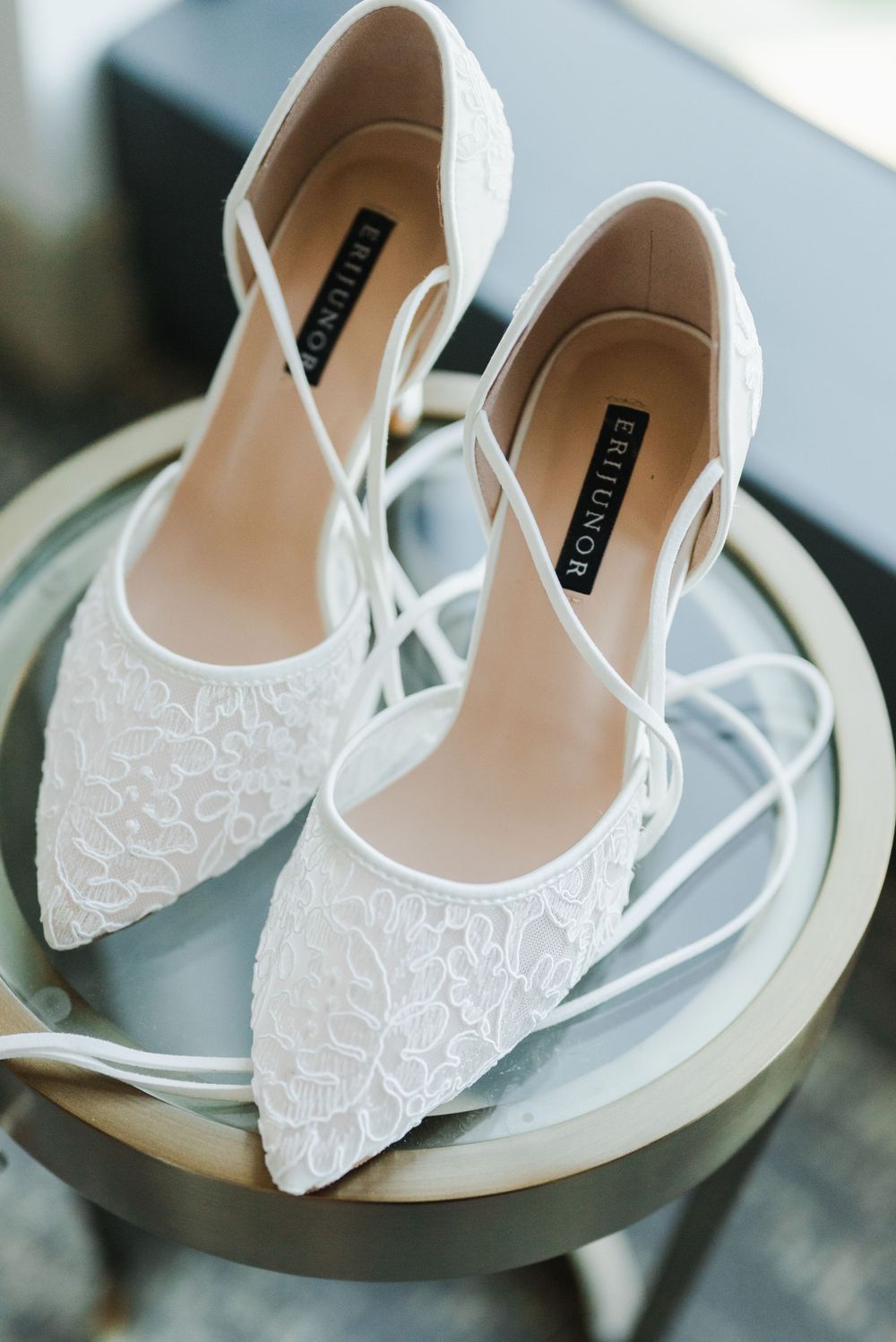 Elegant white lace bridal shoes with pointed toe displayed on reflective surface.