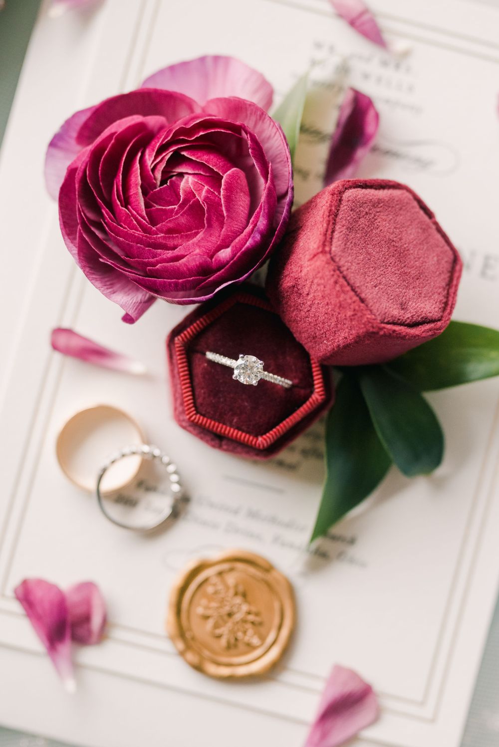 Burgundy velvet ring box with engagement ring and roses on white invitation suite.