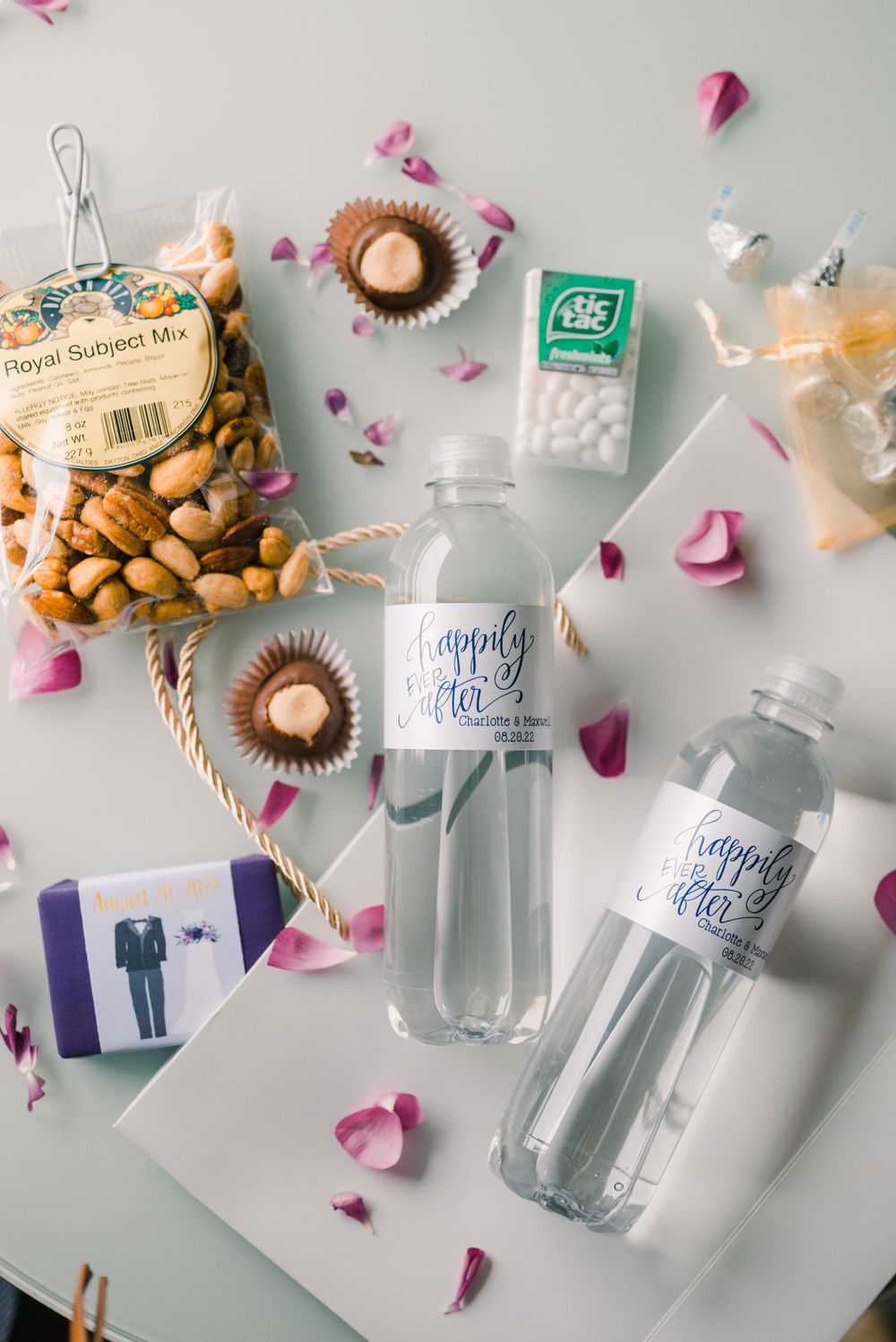 Wedding favors and mini water bottles decorated with custom labels and pink rose petals.