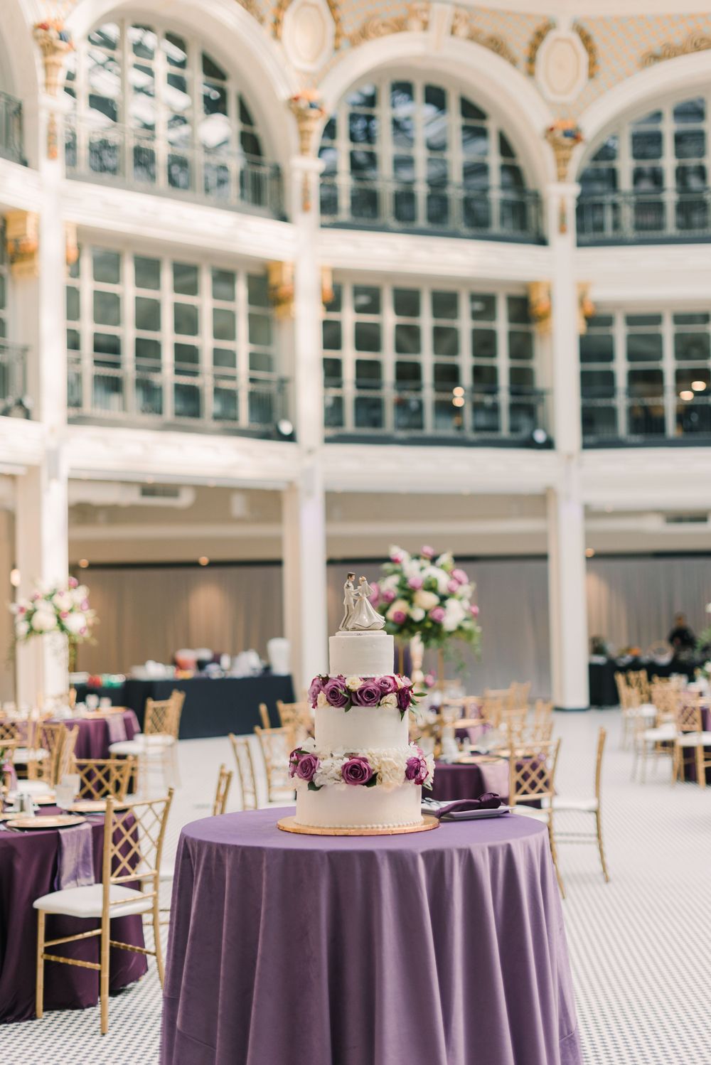 Grand ballroom wedding venue with arched windows, purple tablecloths, and elegant table settings.