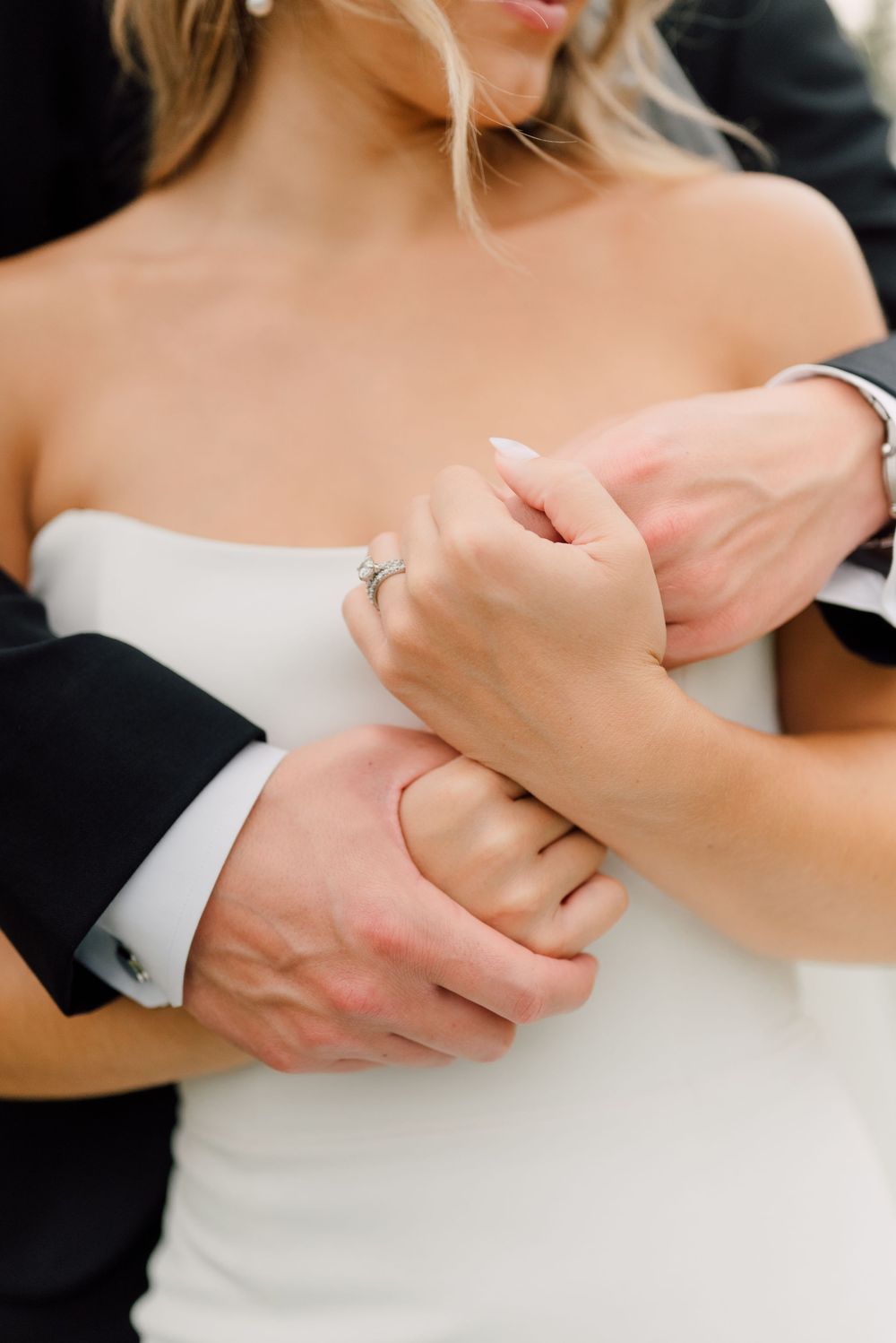 Close-up of couple holding hands showing wedding rings and formal attire.