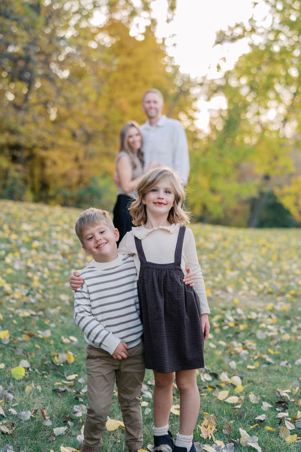 Two children in coordinating outfits play and laugh during a fall photo session.