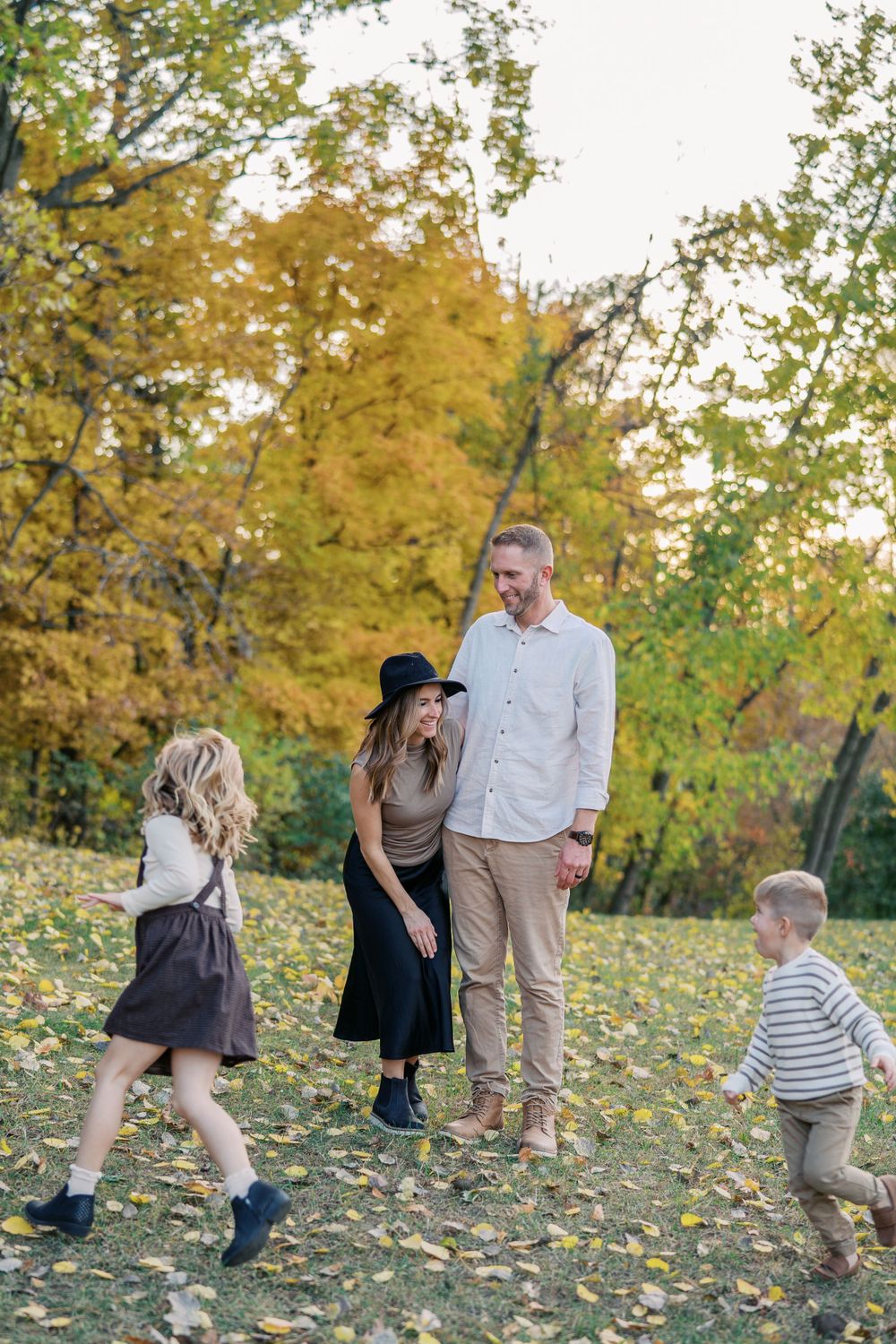Family enjoying playful moments in a field with golden autumn leaves.