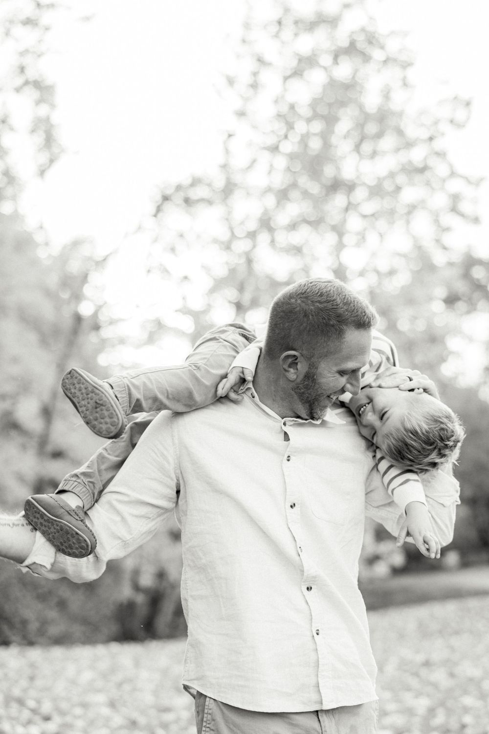 Black and white portrait of playful moments outdoors with autumn trees in background.