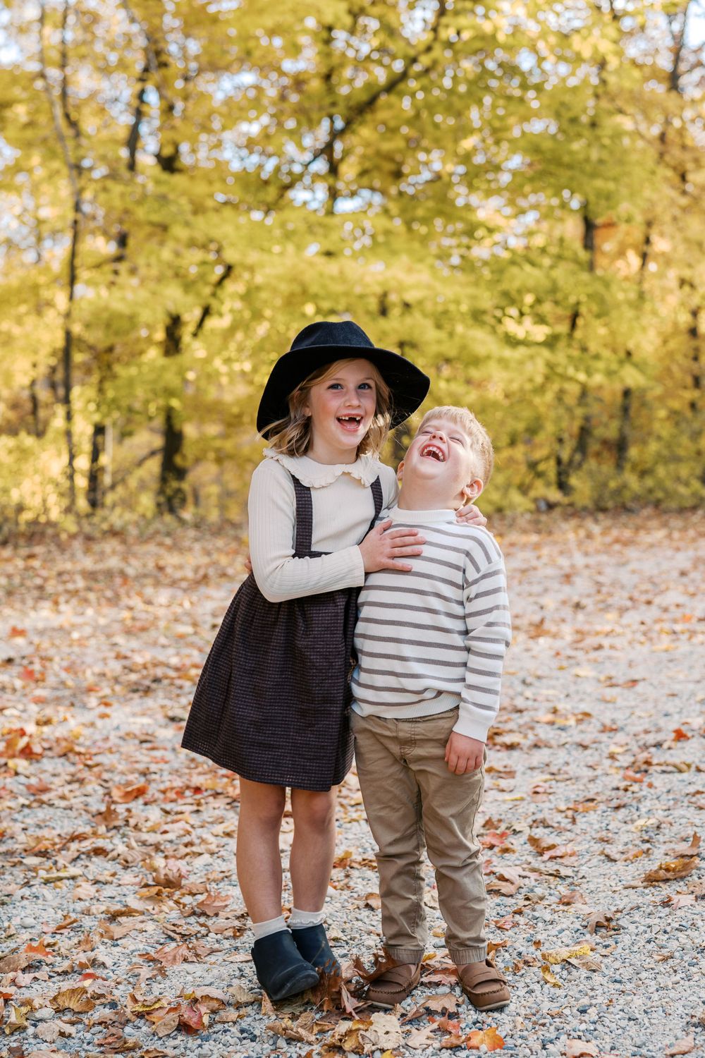 Playful interaction between two people on a leaf-covered forest path during fall.
