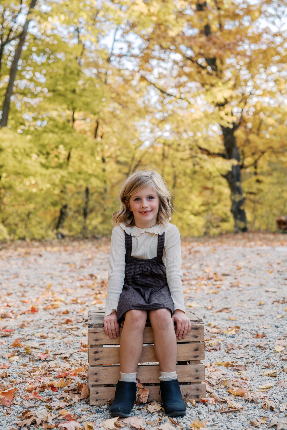 Person sitting on wooden crates surrounded by autumn leaves and golden trees.