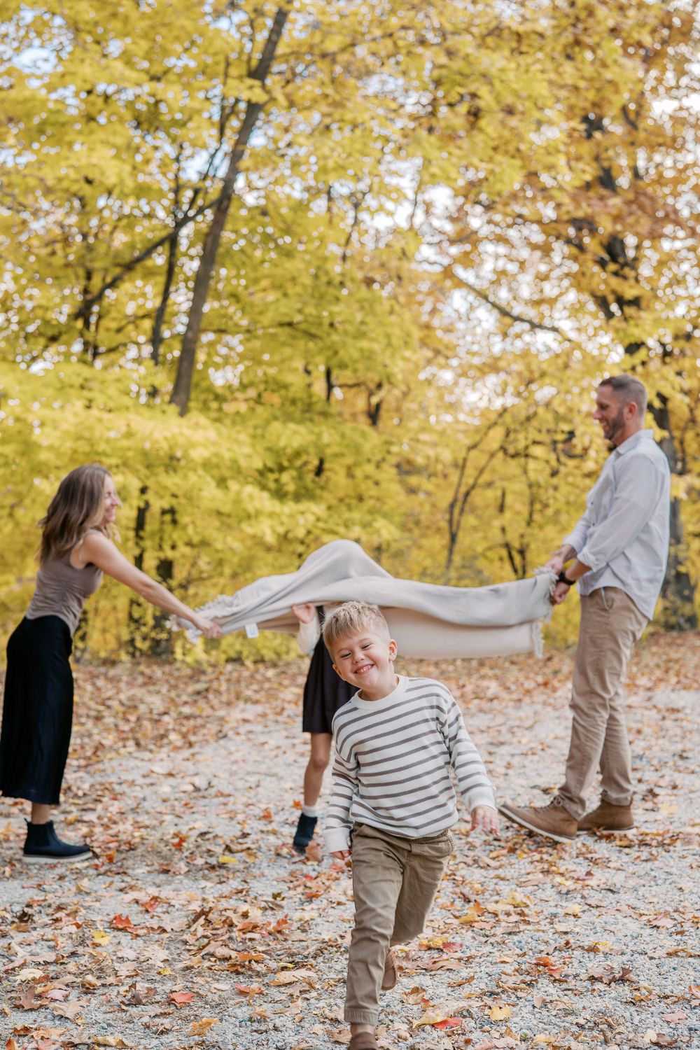 Playful family photo sequence with blanket toss in fall forest setting.