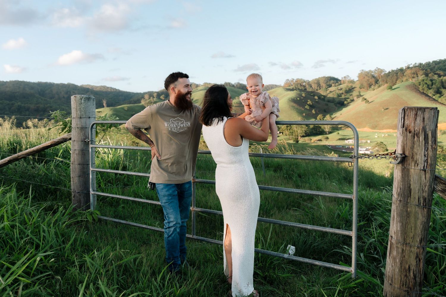 Family standing by rustic fence on rolling green hills during sunset.