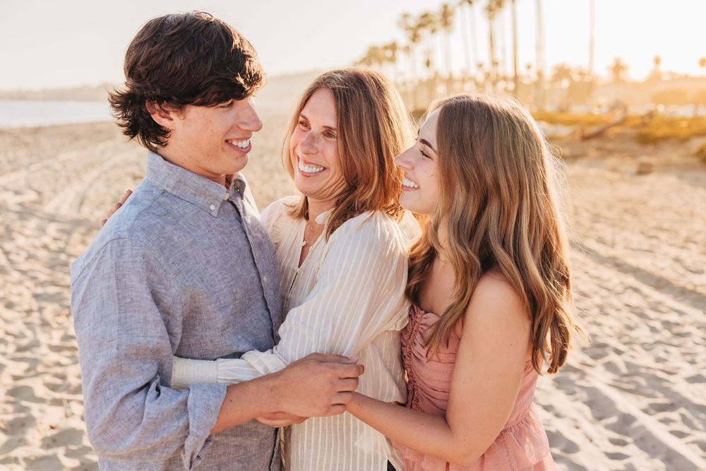 A joyful group embraces on a sunny beach with palm trees and golden light during sunset.