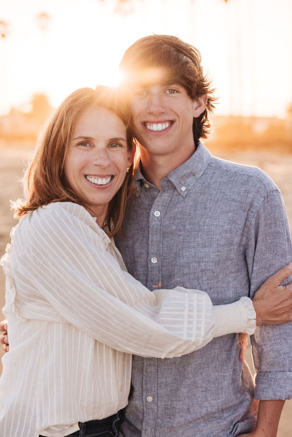 mom hugging high school graduate during senior photoshoot on the beach during golden hour