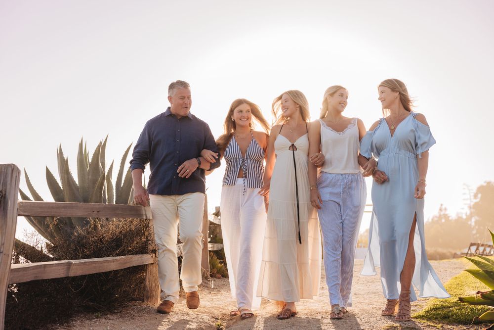 A group walks together along a coastal path during golden hour, wearing casual blue and white outfits.