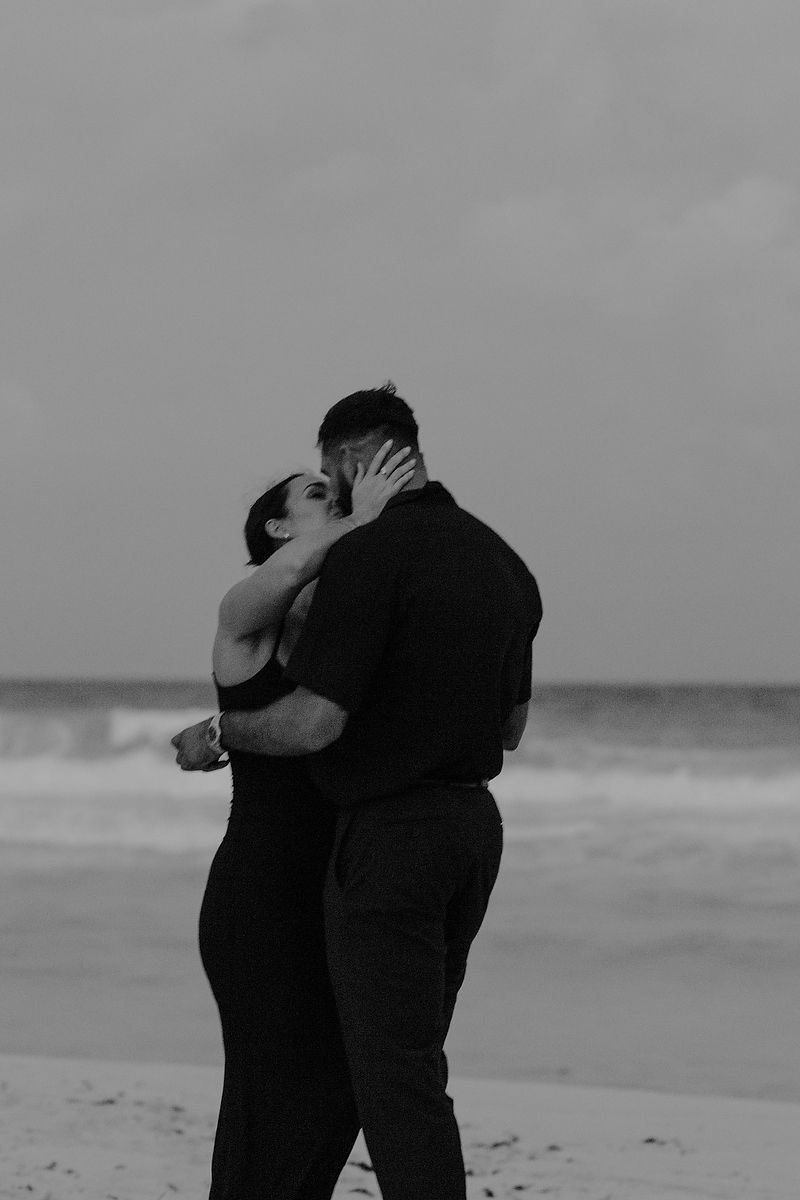 Black-and-white editorial engagement portrait of a couple hugging by the sea in Cancún.
