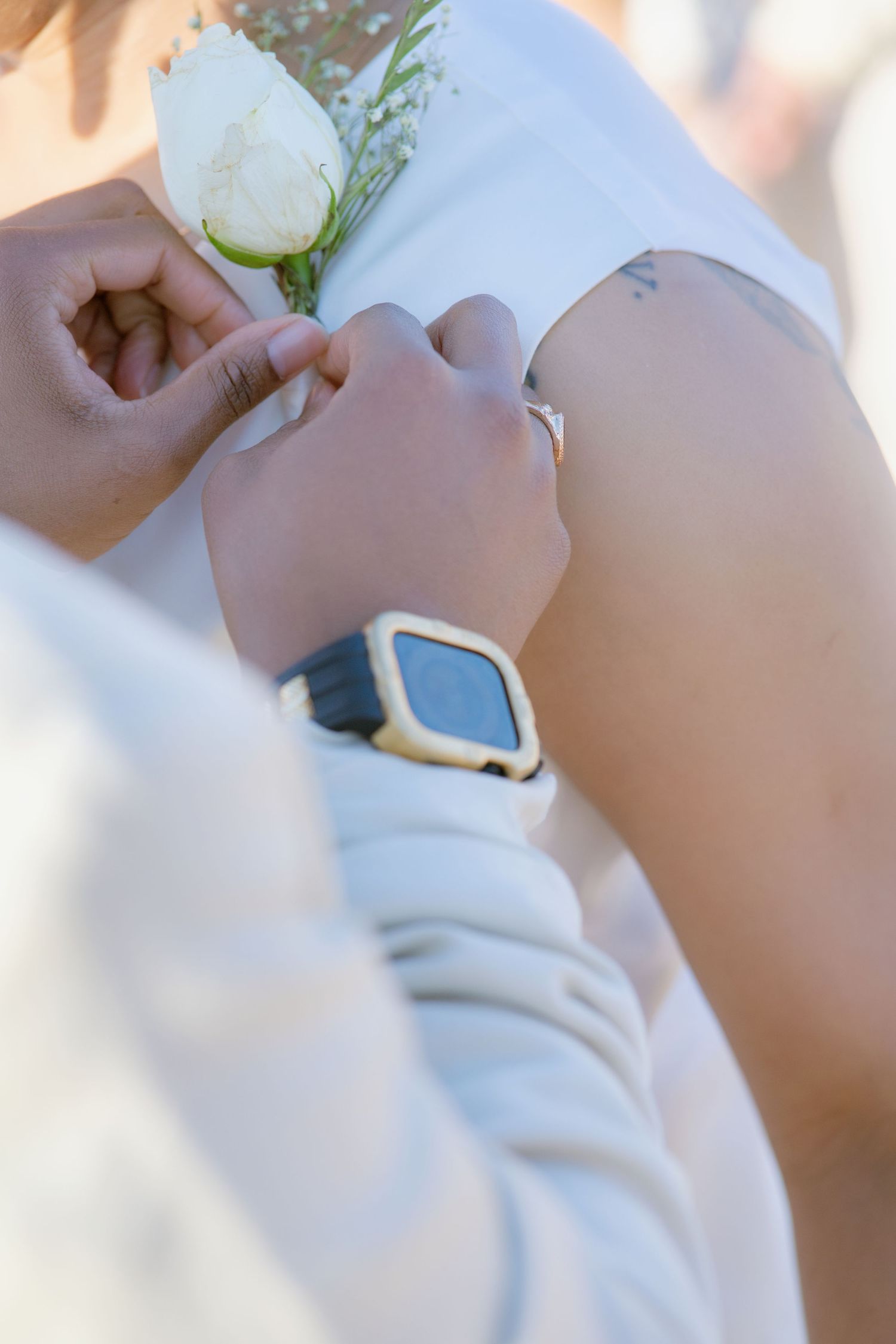 Close-up of hands pinning white boutonniere with smartwatch visible.