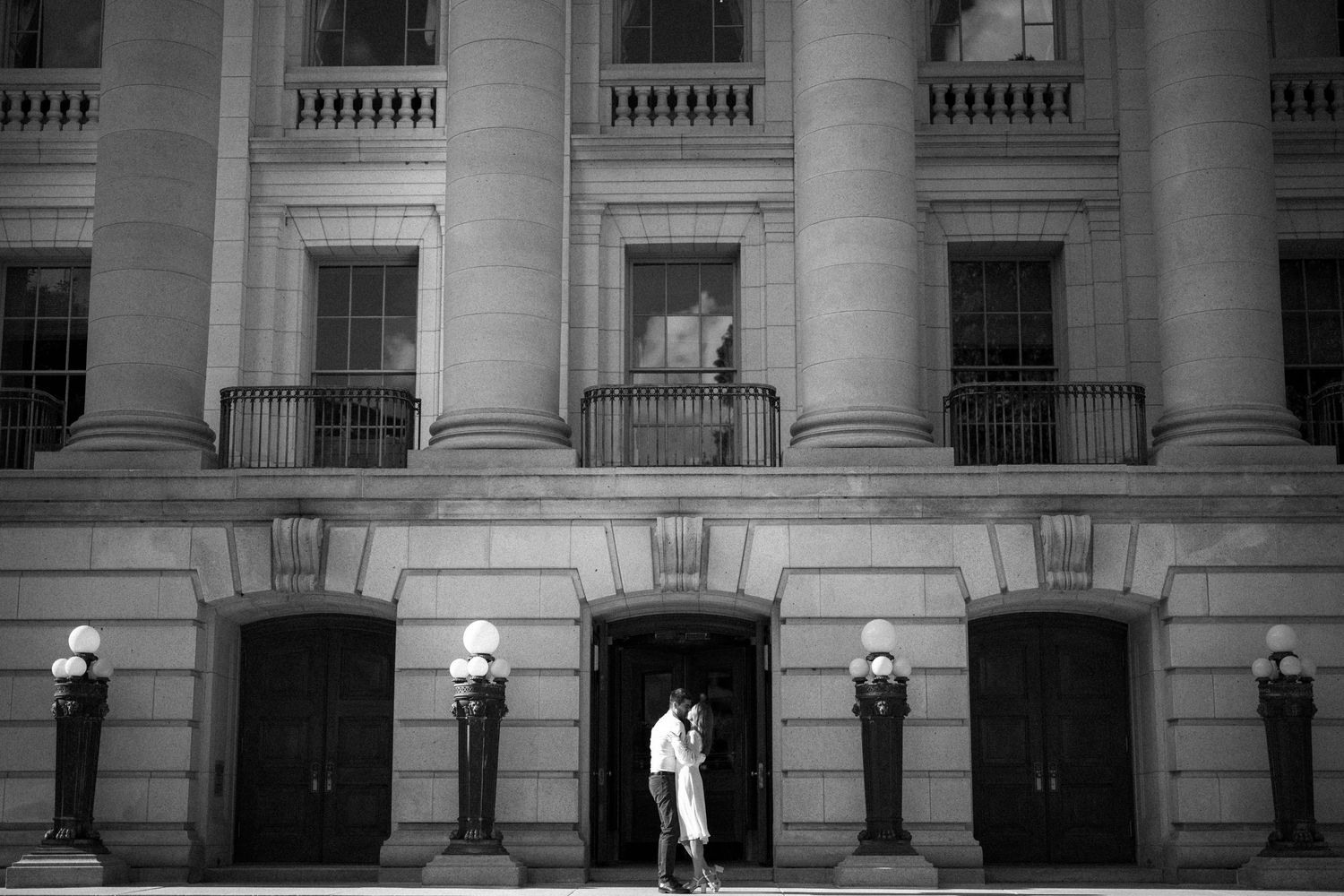 Black and white architectural photograph showing entrance to a grand stone building with columns and wall sconces.