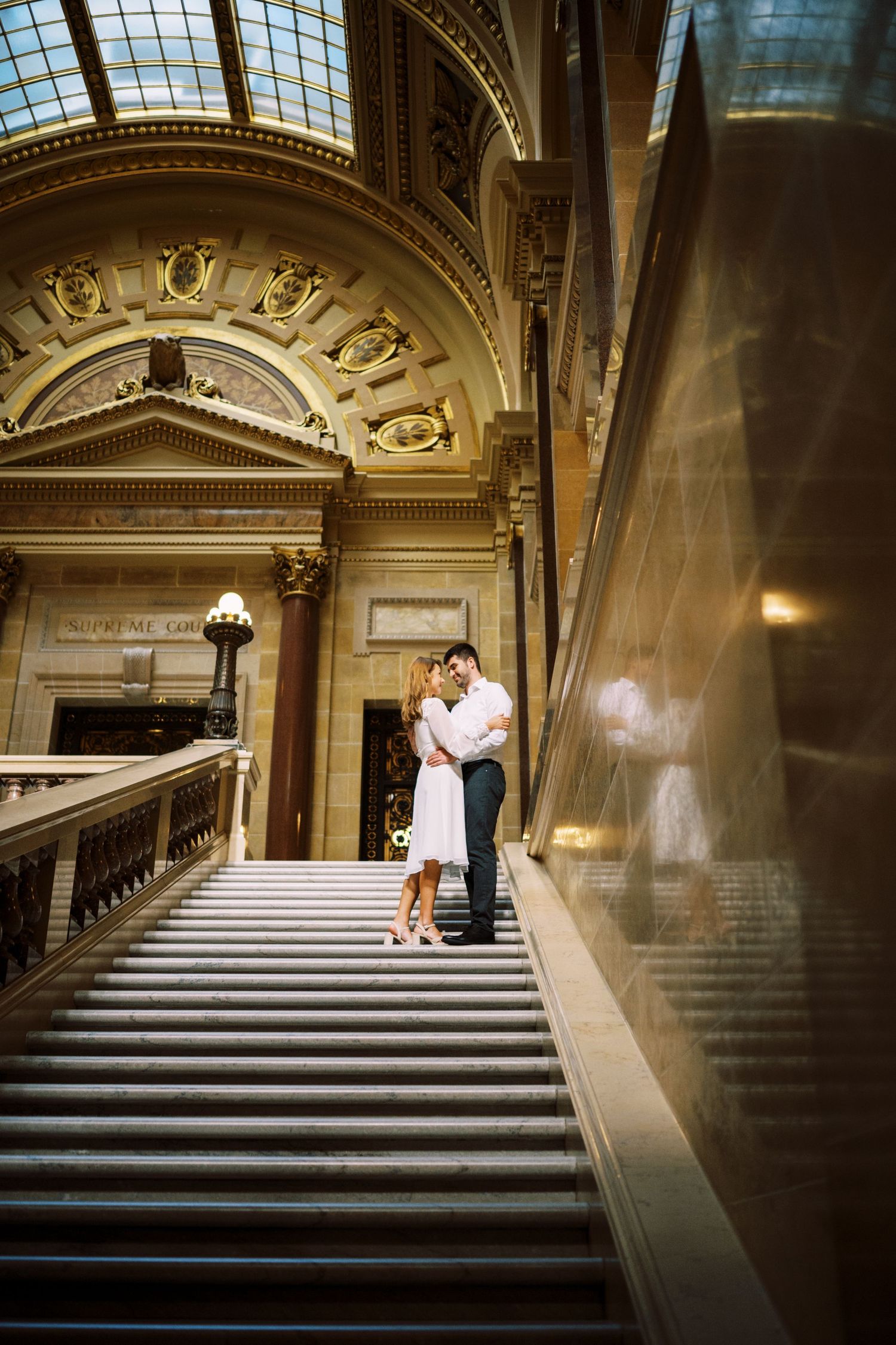 A romantic moment captured on an ornate marble staircase with a domed skylight and classical architectural details.