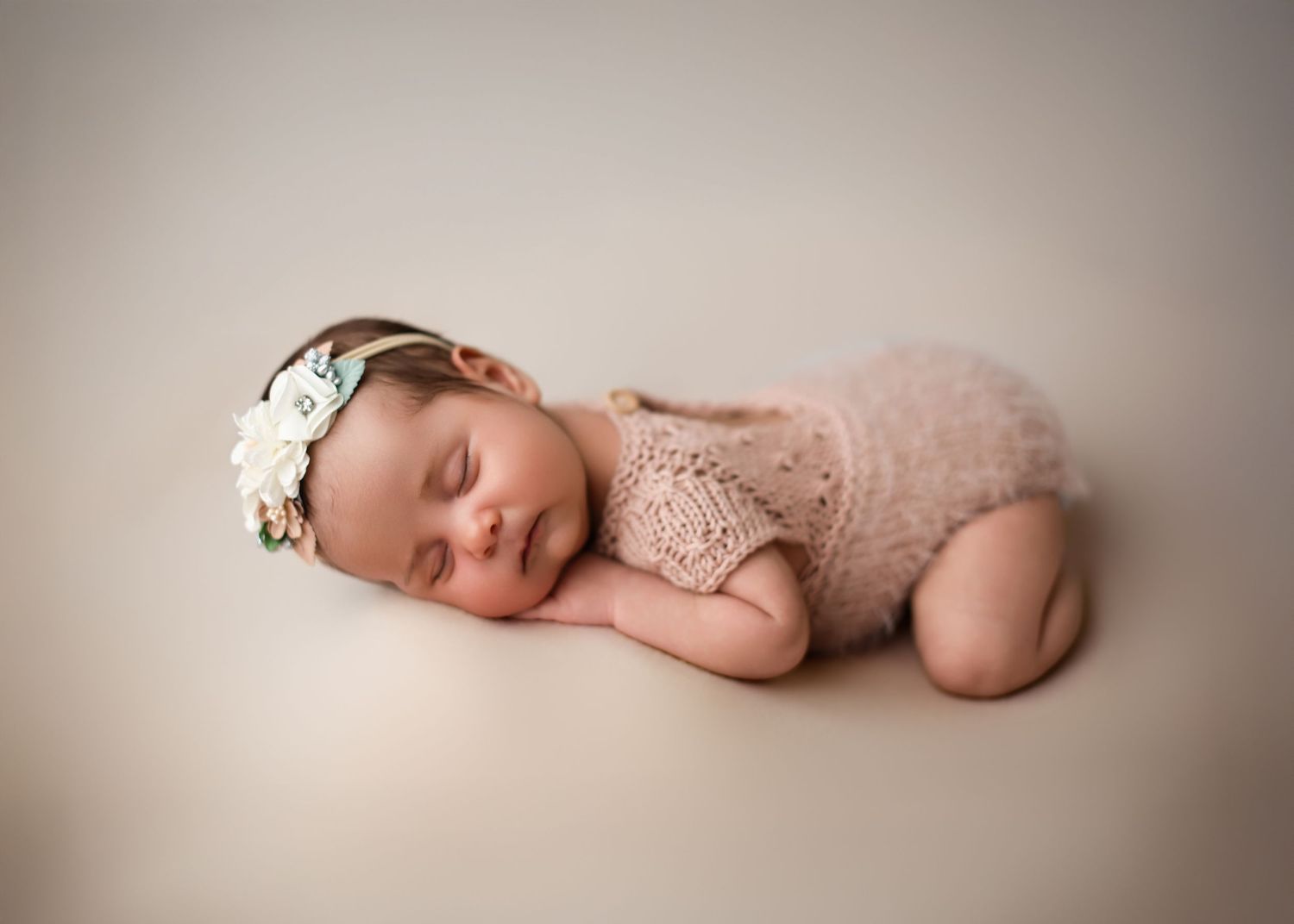 Sleeping newborn wrapped in pink tulle with delicate lace headband lying on soft beige backdrop for portrait session.