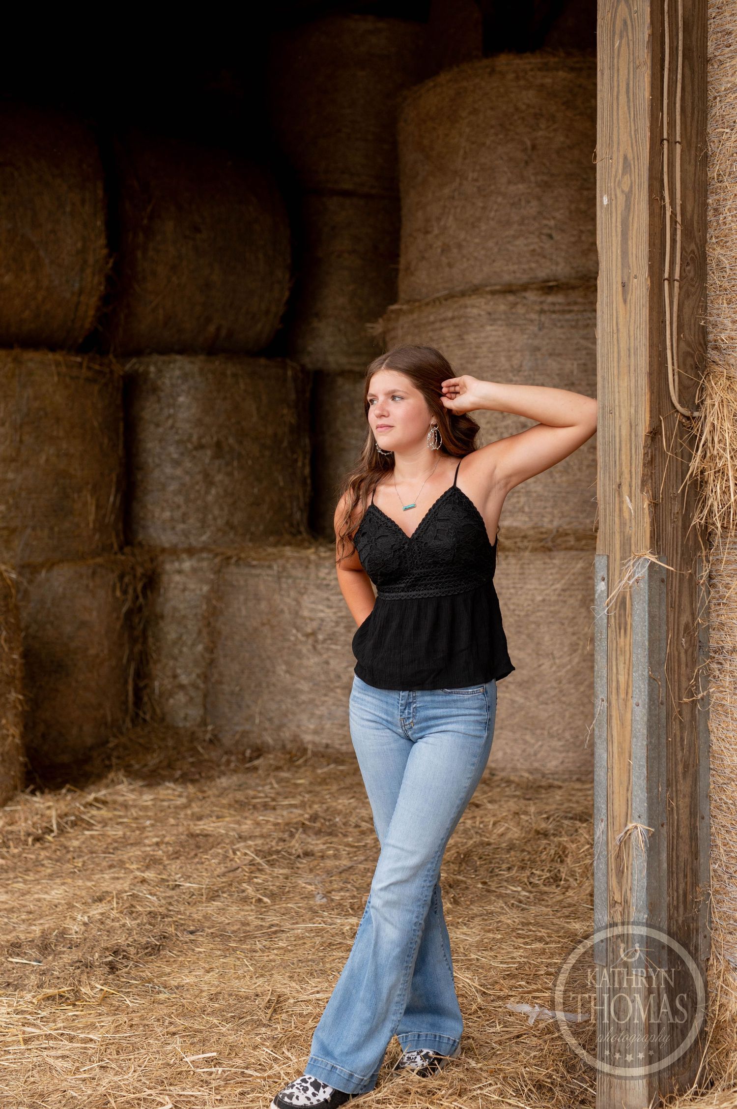 Casual pose against stacked hay bales in rustic barn setting.