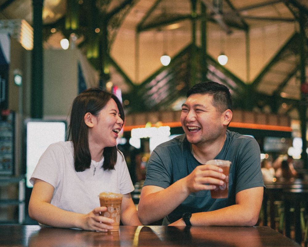 Candid moment of two people laughing while enjoying drinks at a restaurant.