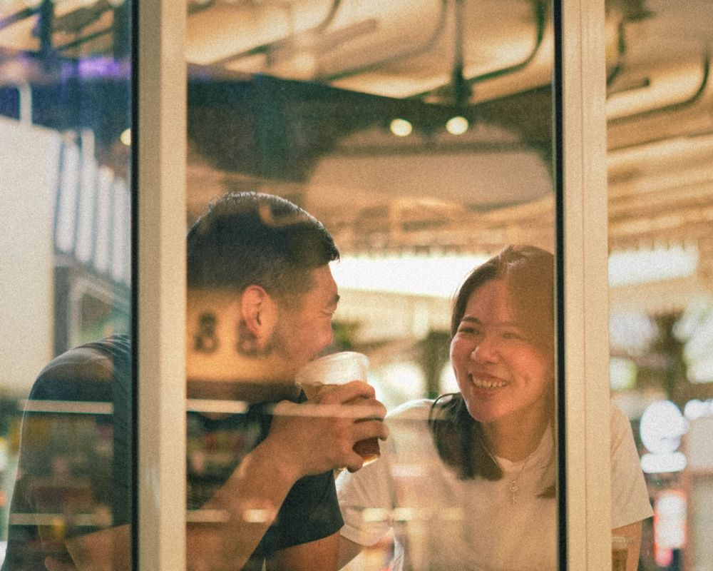Reflection through window glass of two people sharing drinks and conversation.