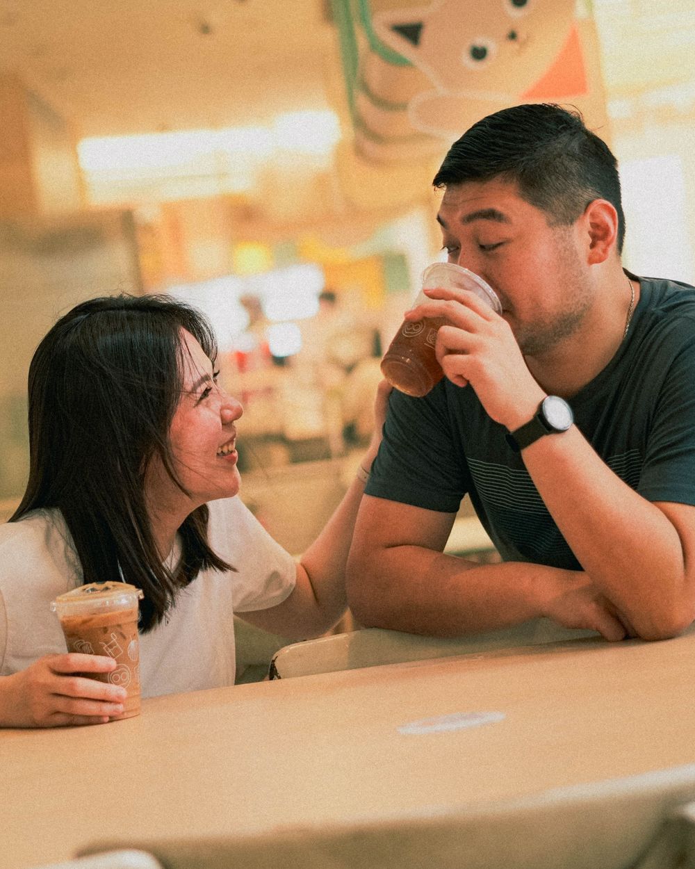 Couple sharing drinks and laughing together at a casual cafe table.