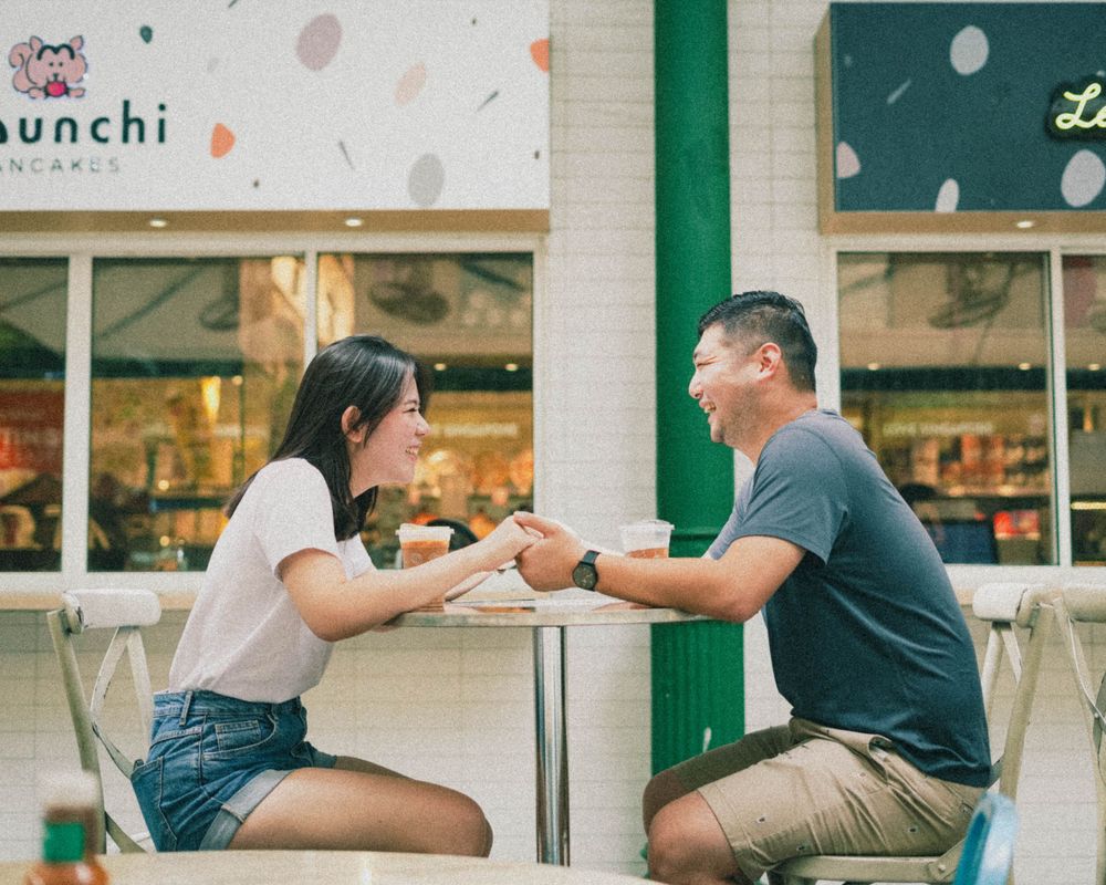 Two people sitting at outdoor cafe table sharing a moment over drinks.