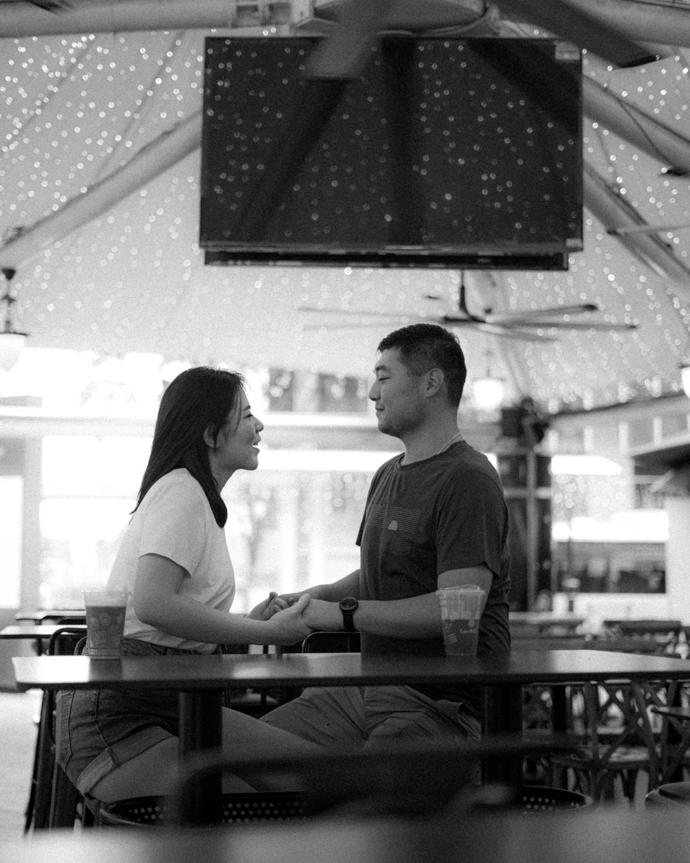 Black and white photo of couple having intimate conversation at cafe table under twinkling lights.