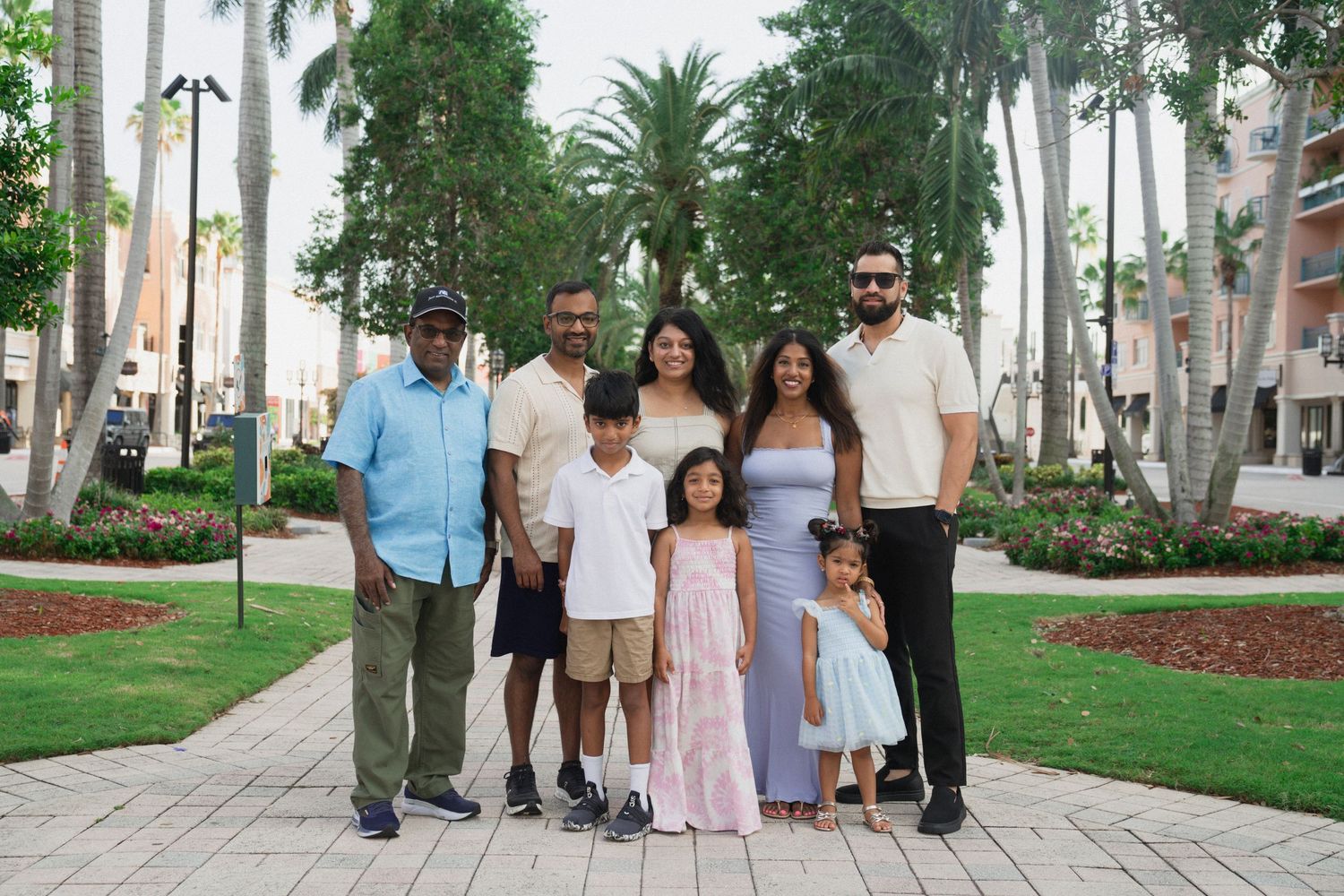 Multi-generational family of seven poses together outdoors among tropical palm trees on a scenic garden pathway.