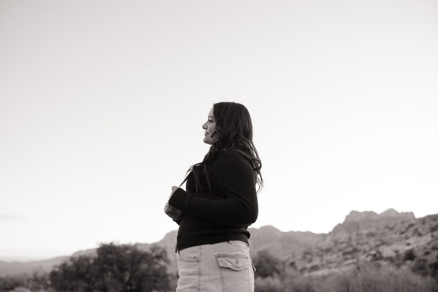 Black and white portrait of a person in casual clothing looking out over a desert landscape in contemplative pose.