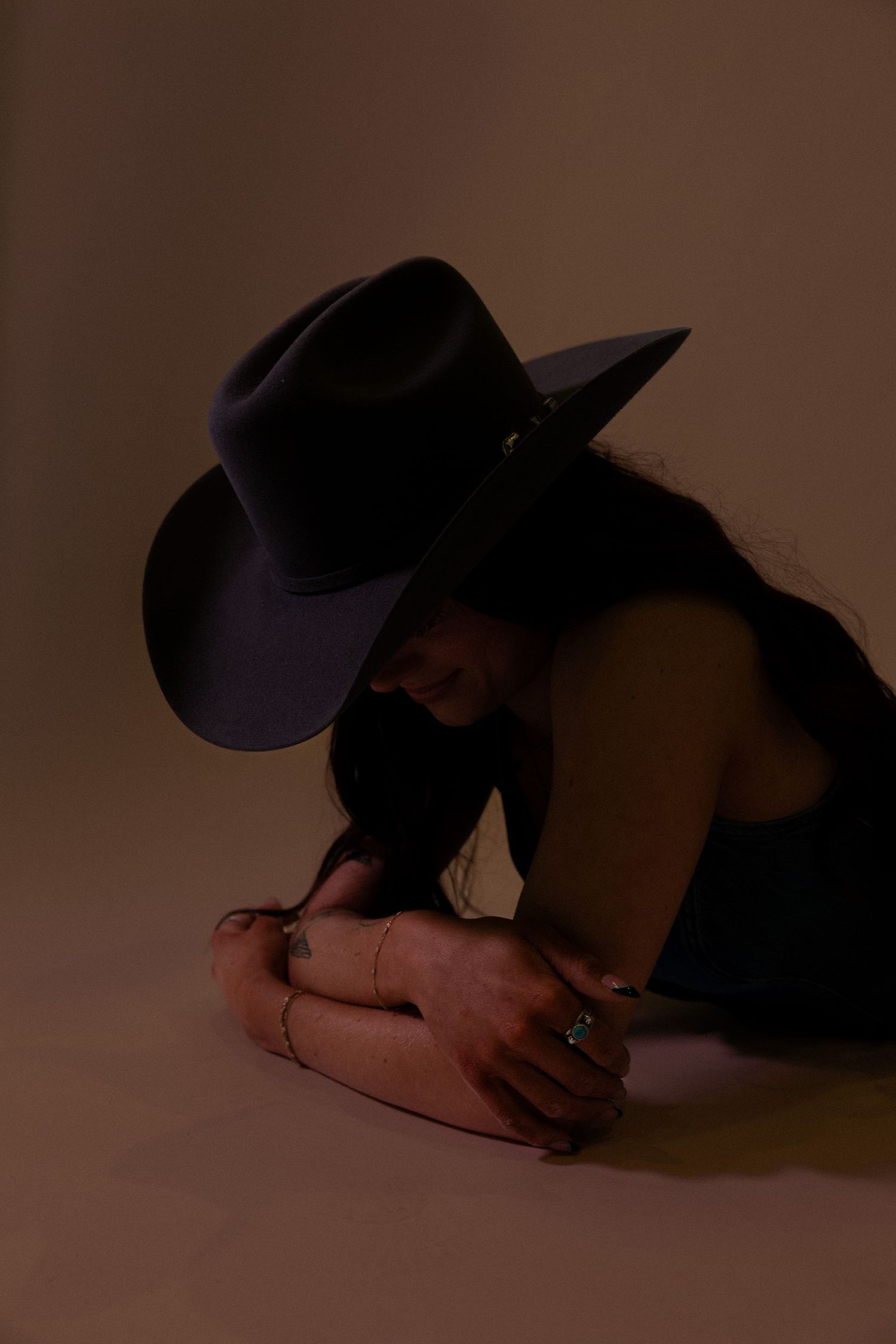Woman in a black cowboy hat posing with crossed arms in warm studio lighting.