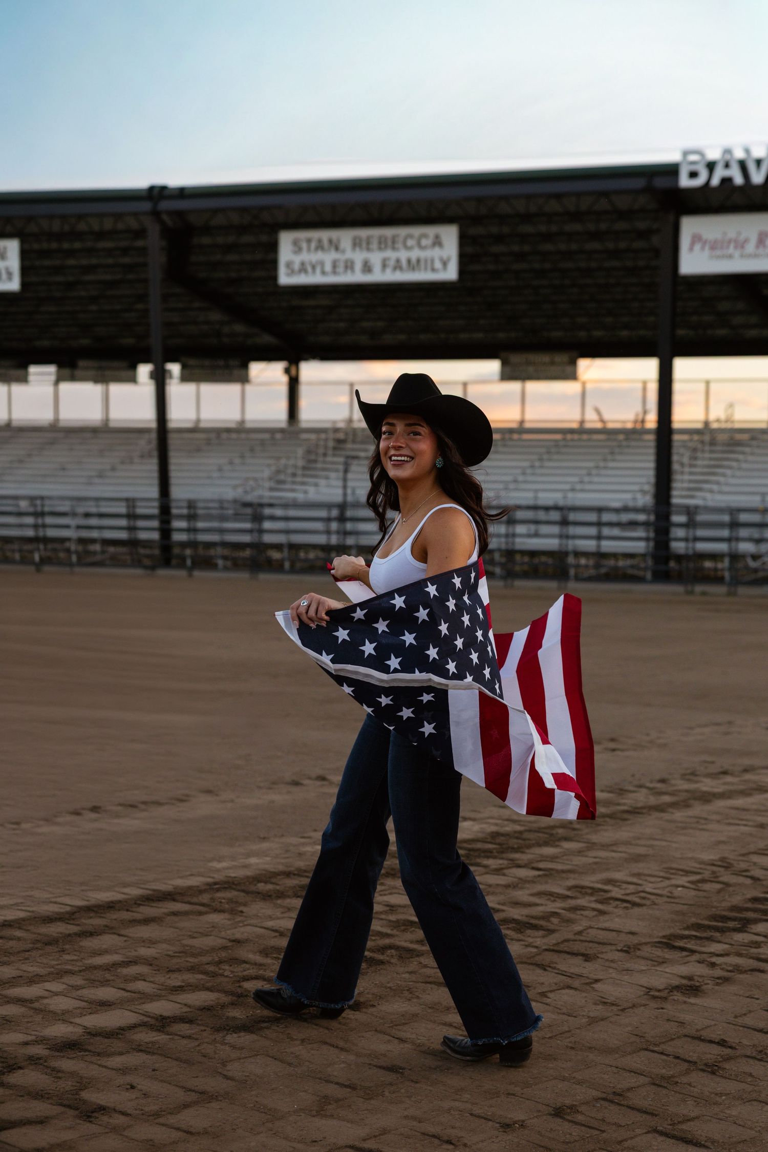 Woman in a black cowboy hat posing with crossed arms in warm studio lighting.