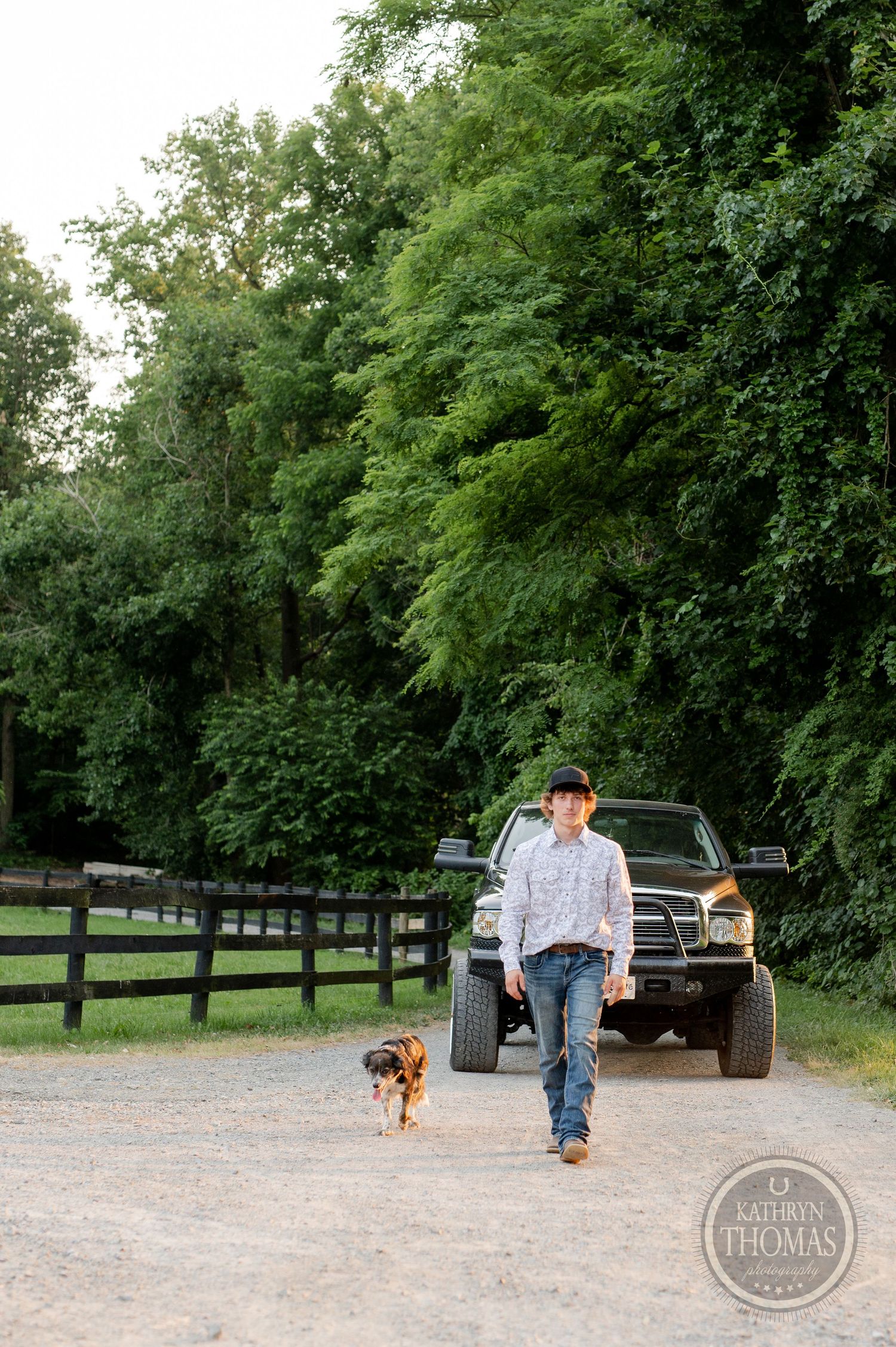 A person walks their dog down a gravel path with a black pickup truck in the background.