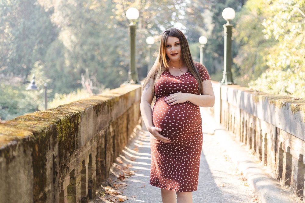 A woman in a polka dot dress poses in a golden sunlit outdoor setting on a rustic bridge walkway.