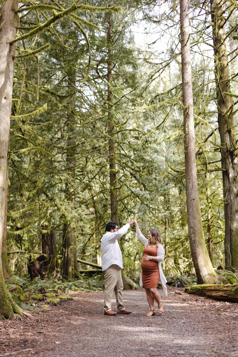 Two people high-five each other while walking on a forest trail surrounded by tall evergreen trees.