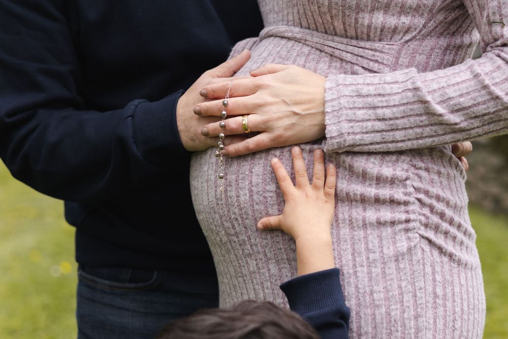 Close-up shots of hands holding a pregnant belly in a ribbed sweater against a blurred outdoor background.