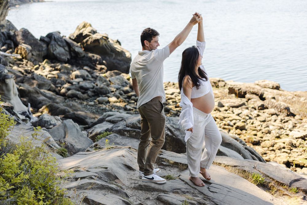 A couple dances together on rocky coastal terrain during a sunset photoshoot by the water.