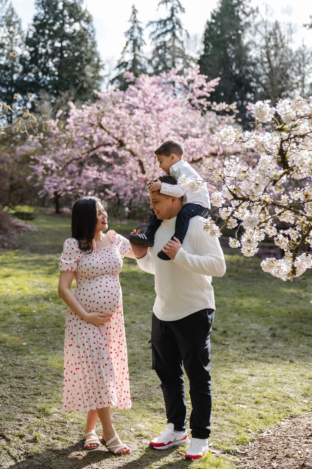 A family poses together under blooming cherry blossom trees in a spring garden setting.