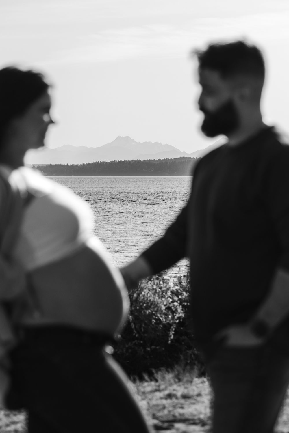 Silhouettes of a couple against a scenic ocean backdrop with mountains in the distance.