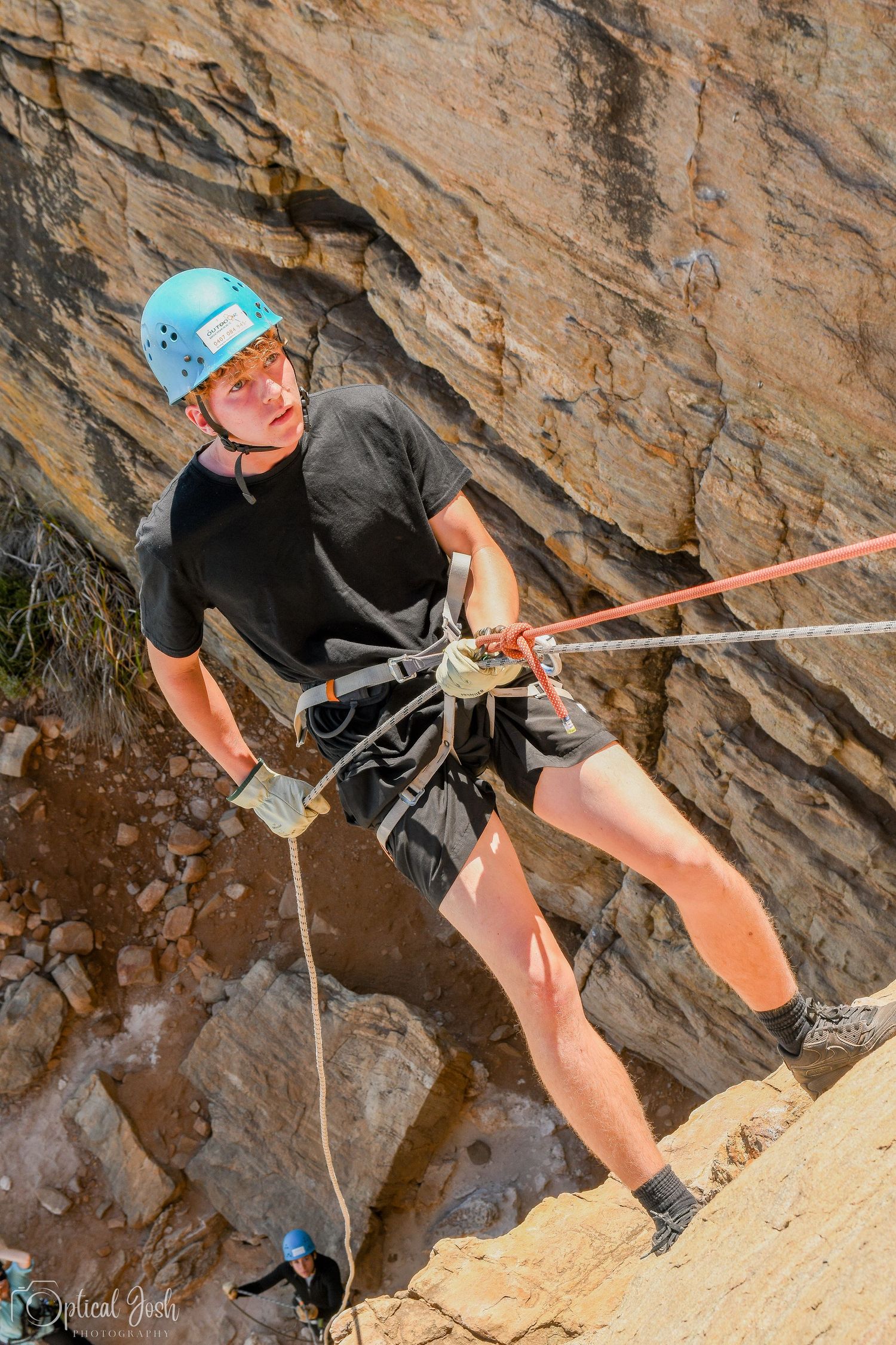 Rock climber in safety gear rappelling down steep rocky cliff face.