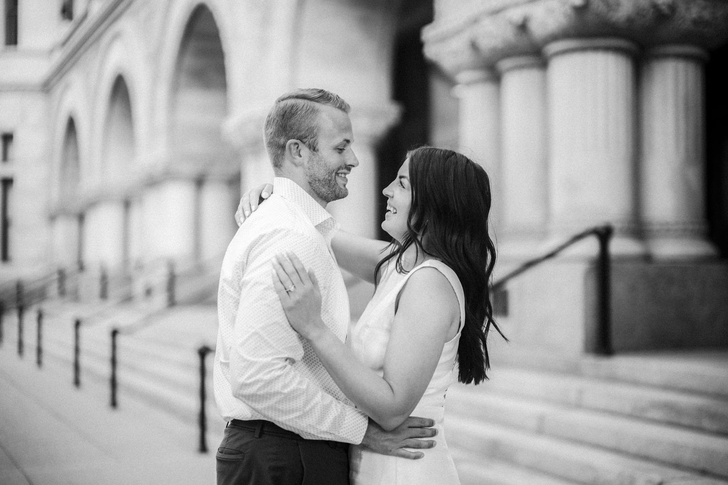 A romantic black and white portrait of a couple embracing in front of a classic architectural building with columns.
